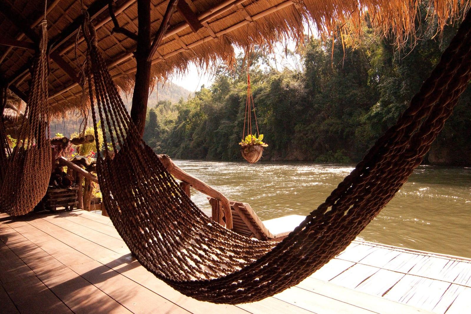 A hammock on a thatched riverside deck overlooking a jungle river.